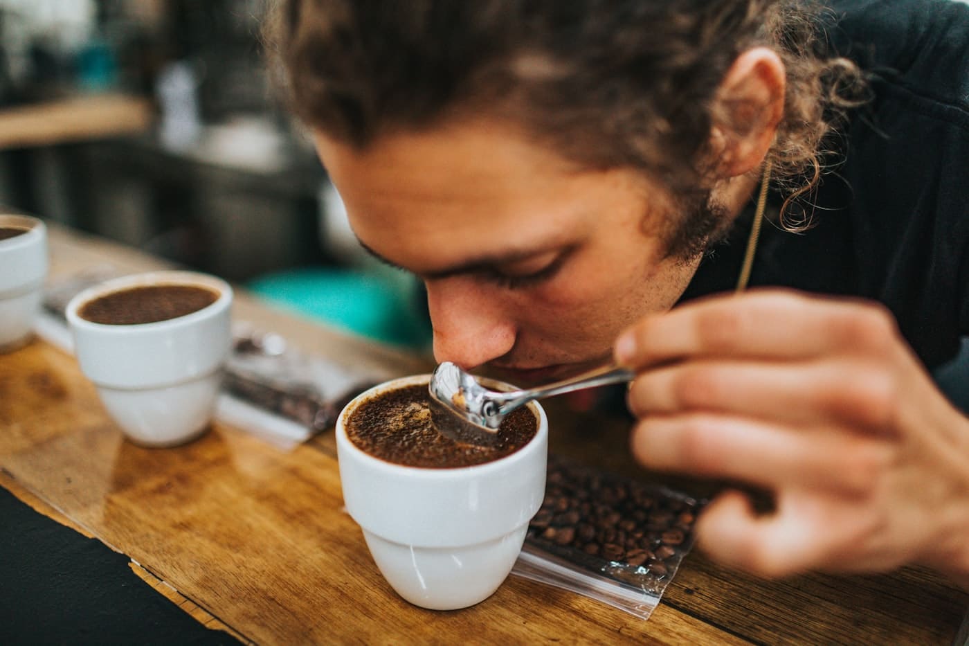 A cupper leaning over a bowl, drawing coffee off the spoon.