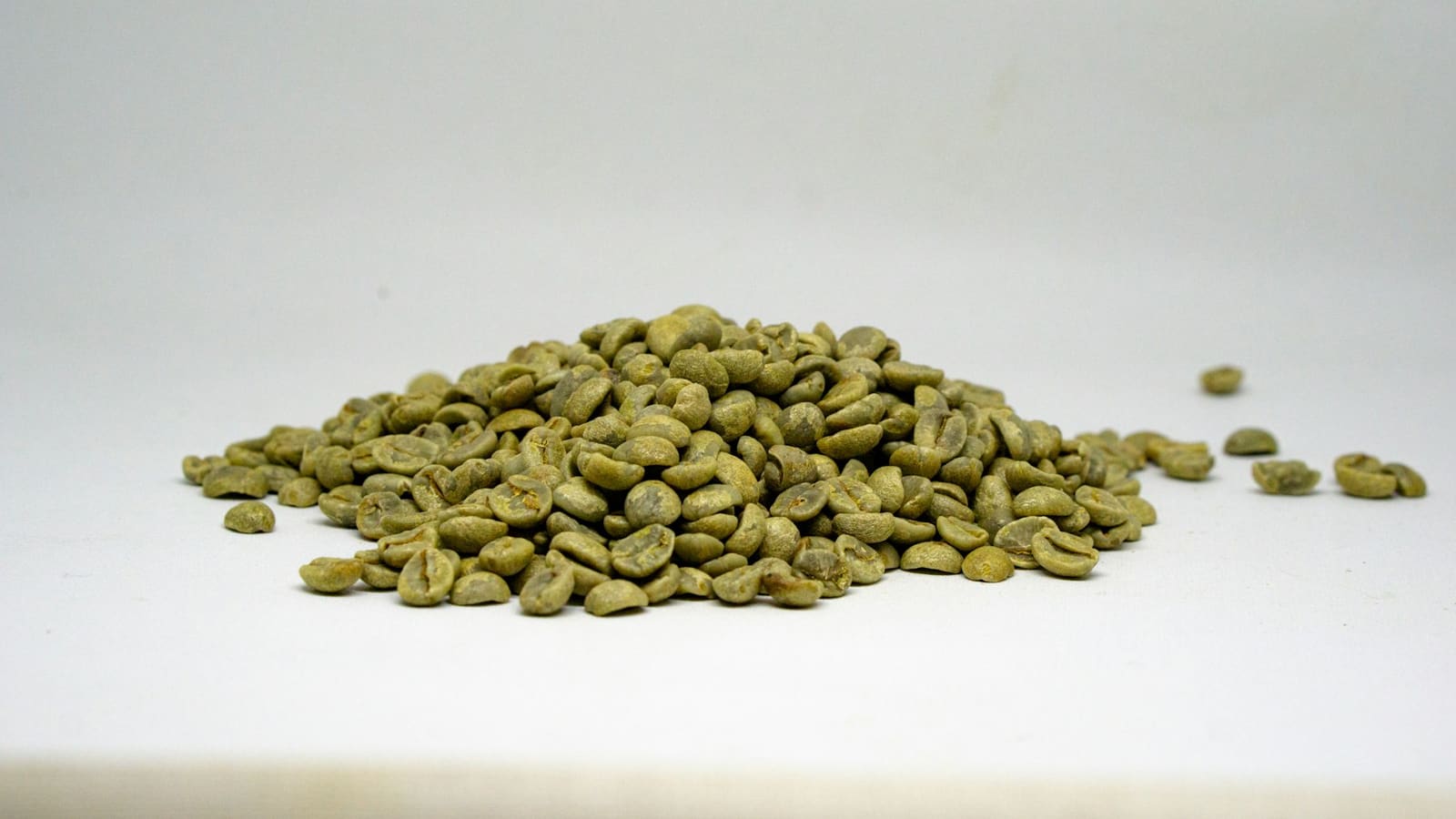 A heap of unroasted coffee beans, olive-green, on a white surface.