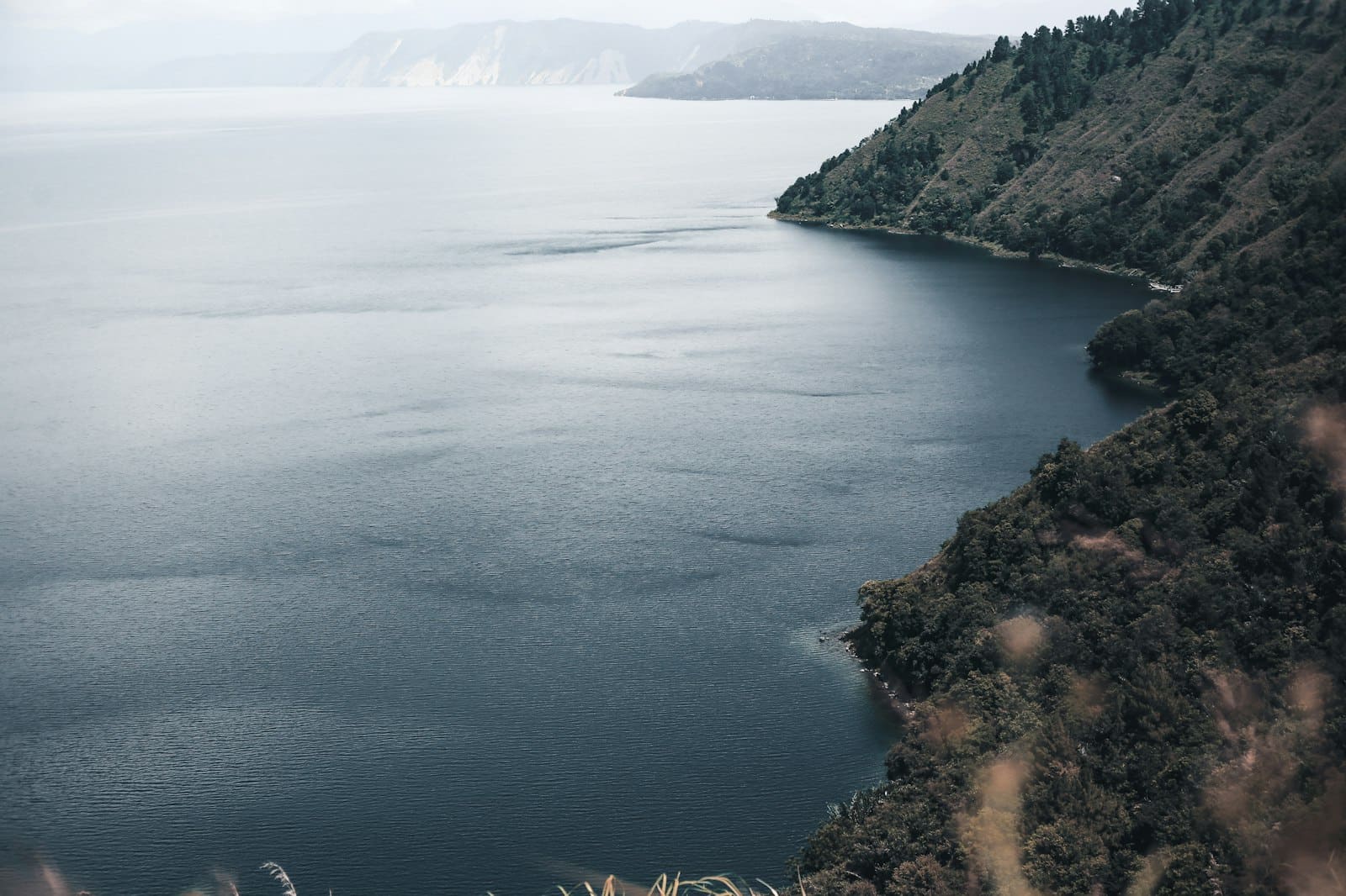 A still lake lying against a steep forested hill.